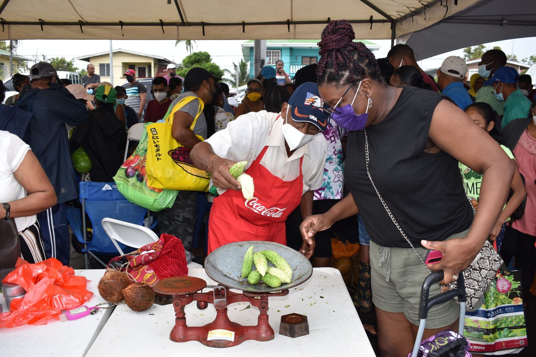A vendor weighs bora on a red market scale for a customer at a busy outdoor market